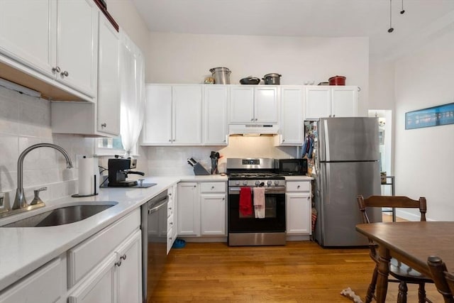 kitchen with stainless steel appliances, a sink, under cabinet range hood, and white cabinetry