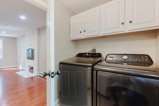 laundry area featuring washing machine and dryer, cabinet space, light wood-style floors, baseboards, and a fireplace