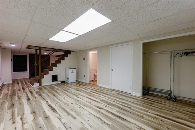 finished basement featuring stairs, light wood finished floors, a drop ceiling, and baseboards