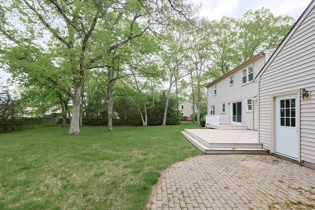 view of grassy yard featuring a wooden deck and a patio area
