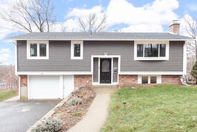 bi-level home featuring driveway, a front lawn, a shingled roof, a garage, and a chimney