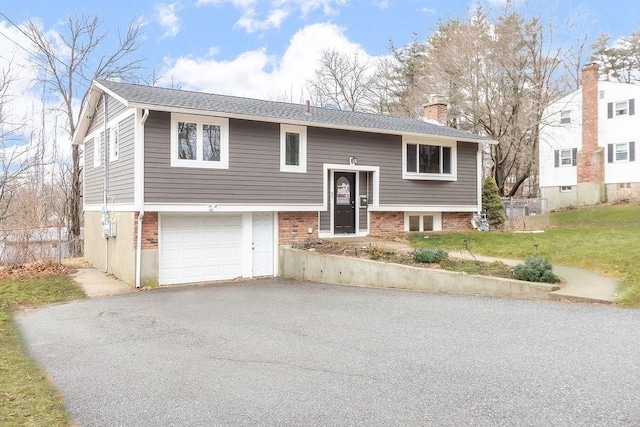 split foyer home with aphalt driveway, a front yard, a garage, brick siding, and a chimney