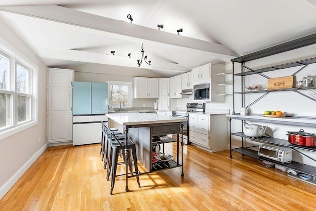 kitchen featuring vaulted ceiling with beams, white cabinets, under cabinet range hood, appliances with stainless steel finishes, and a kitchen bar