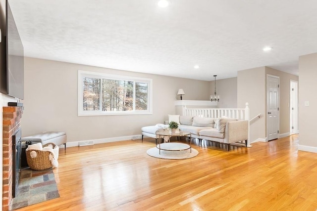 living room featuring visible vents, wood finished floors, baseboards, a brick fireplace, and a chandelier