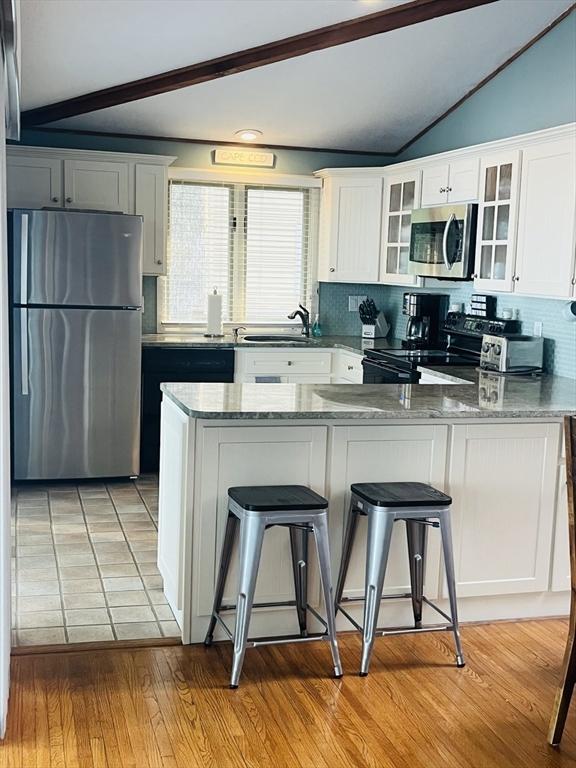 233 Hoopdole Rd, Mashpee, MA 02649 - kitchen with stainless steel appliances, a peninsula, tasteful backsplash, glass insert cabinets, and white cabinets