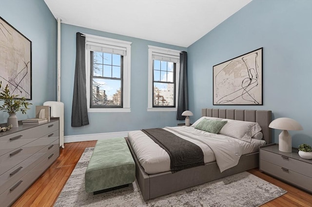 bedroom featuring lofted ceiling, radiator heating unit, and light hardwood / wood-style floors