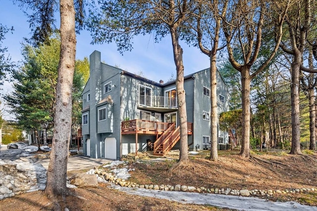 back of property with a balcony, a garage, driveway, stairway, and a chimney