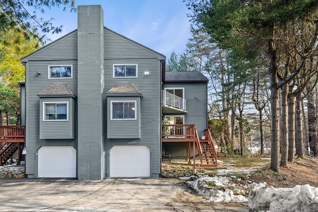 back of house featuring a garage, driveway, a chimney, stairway, and a wooden deck