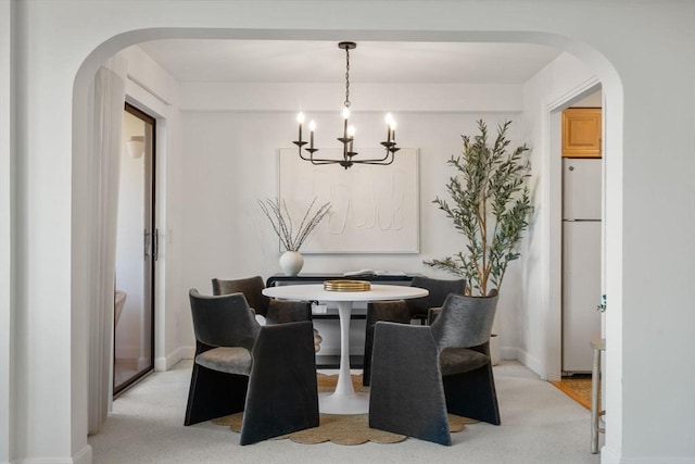 dining area with arched walkways, a chandelier, baseboards, and light colored carpet