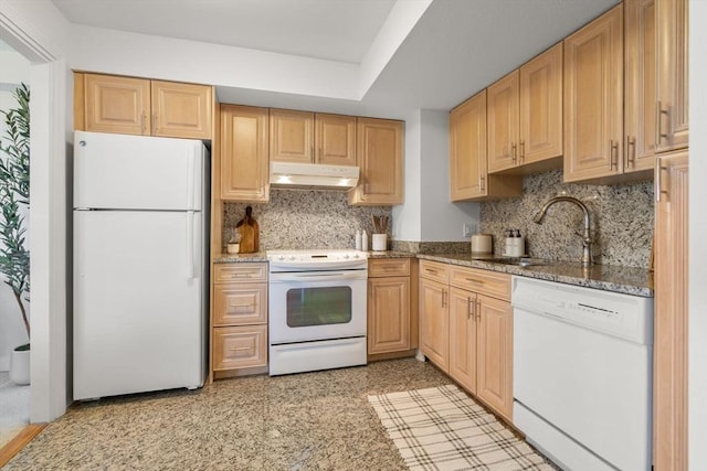 kitchen featuring white appliances, a sink, under cabinet range hood, backsplash, and dark stone countertops