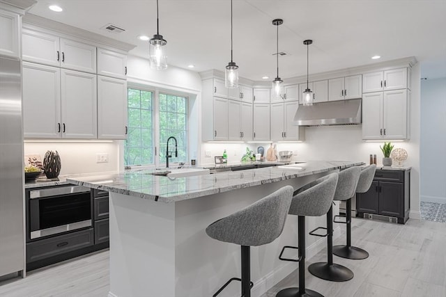 261 E St, Foxboro, MA 02035 - kitchen with under cabinet range hood, white cabinetry, recessed lighting, light stone counters, and a breakfast bar area