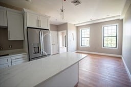 kitchen featuring pendant lighting, white cabinetry, light hardwood / wood-style floors, and stainless steel fridge