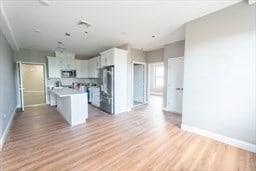 kitchen with light wood-type flooring, stainless steel refrigerator, white cabinetry, and a kitchen island