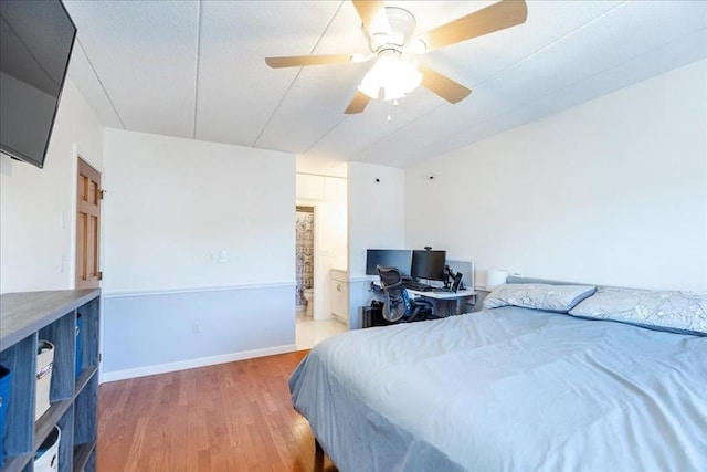 bedroom featuring wood finished floors, a ceiling fan, ensuite bath, and baseboards