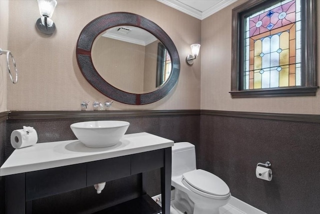 half bathroom featuring vanity, ornamental molding, wainscoting, visible vents, and toilet