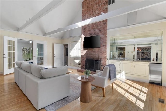 living area with beam ceiling, a brick fireplace, french doors, light wood-type flooring, and visible vents