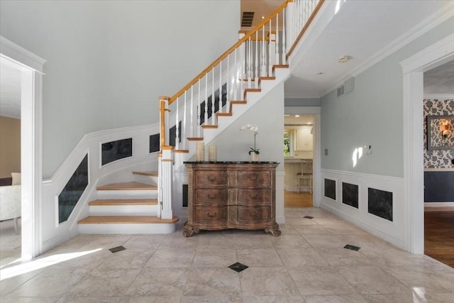 staircase with crown molding, a wainscoted wall, a decorative wall, and visible vents