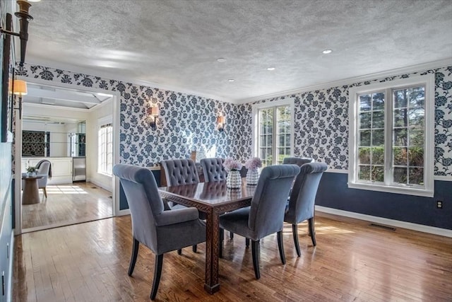 dining area featuring wood-type flooring, wallpapered walls, visible vents, and ornamental molding