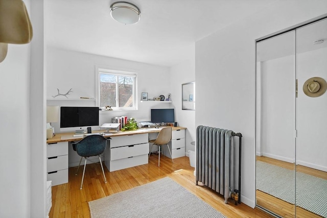 office with built in desk, wood-type flooring, and radiator heating unit