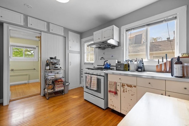 kitchen with under cabinet range hood, light wood finished floors, white gas range oven, light countertops, and white cabinets