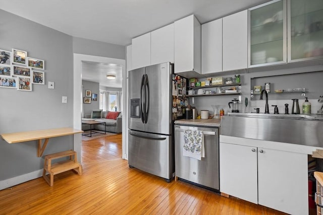 kitchen featuring a sink, open shelves, light wood-style floors, stainless steel appliances, and white cabinets