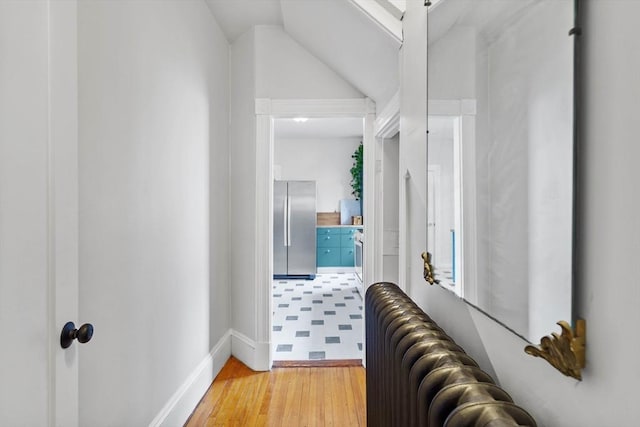 hall with lofted ceiling, radiator, baseboards, and light wood-style floors