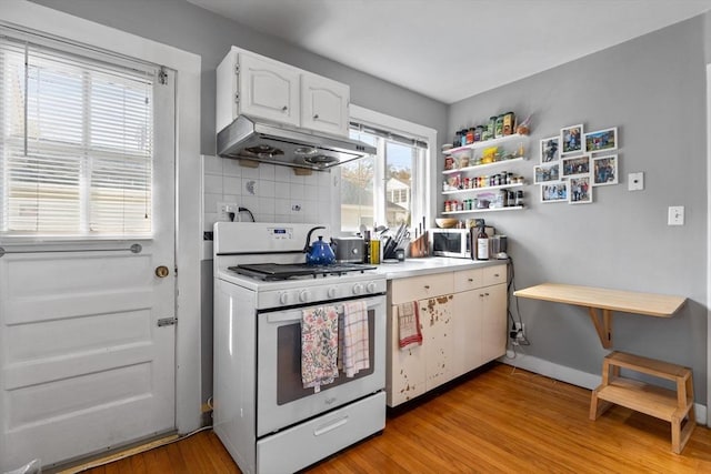 kitchen with under cabinet range hood, white cabinets, decorative backsplash, gas range gas stove, and light wood-type flooring