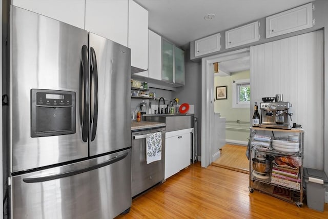 kitchen featuring a sink, stainless steel appliances, light wood-style flooring, white cabinetry, and glass insert cabinets