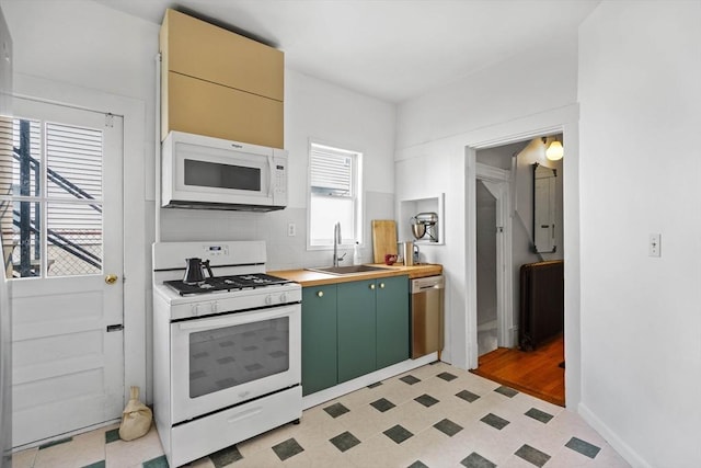 kitchen featuring a sink, white appliances, green cabinetry, light floors, and baseboards