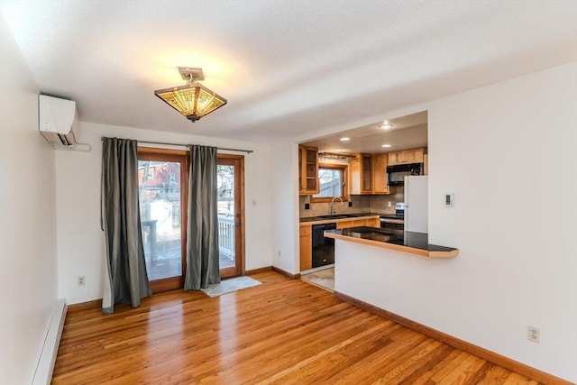 kitchen with a baseboard heating unit, an AC wall unit, light wood-style floors, black appliances, and a sink