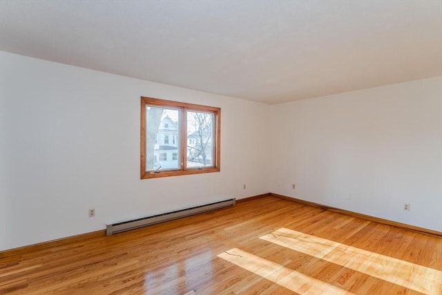 spare room with a baseboard heating unit, baseboards, and light wood-style floors