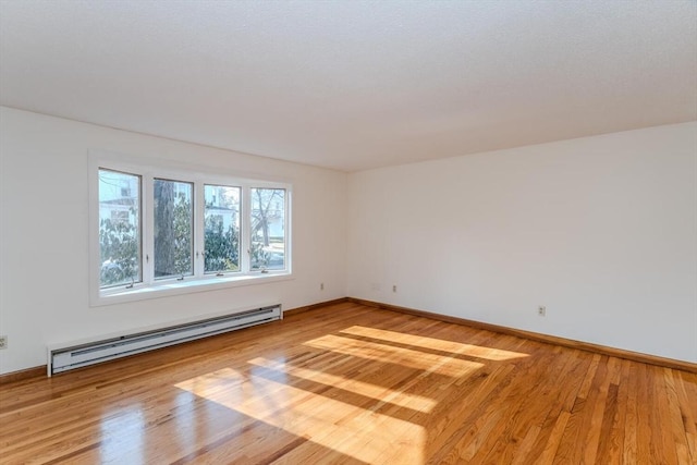 empty room featuring light wood-style flooring, a baseboard heating unit, and baseboards