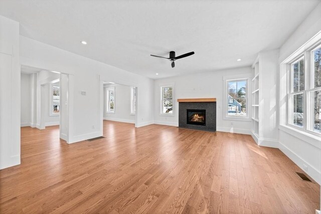 unfurnished living room with visible vents, baseboards, a ceiling fan, a fireplace with flush hearth, and light wood-type flooring