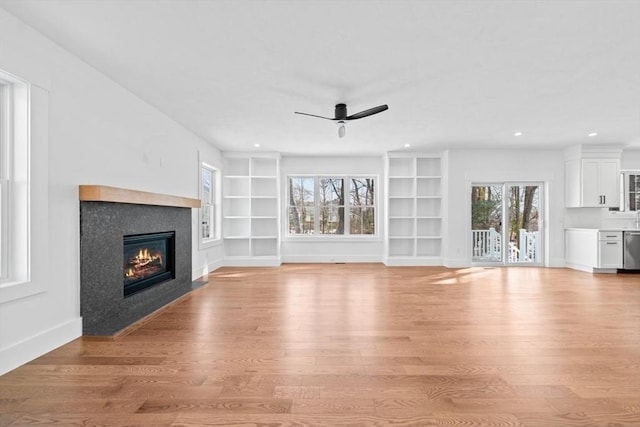 unfurnished living room featuring built in features, baseboards, a ceiling fan, light wood-style flooring, and a fireplace with flush hearth