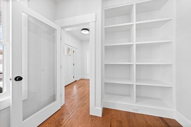 hallway with built in shelves, plenty of natural light, and wood finished floors