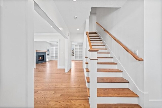 stairs with recessed lighting, wood finished floors, baseboards, built in features, and a lit fireplace