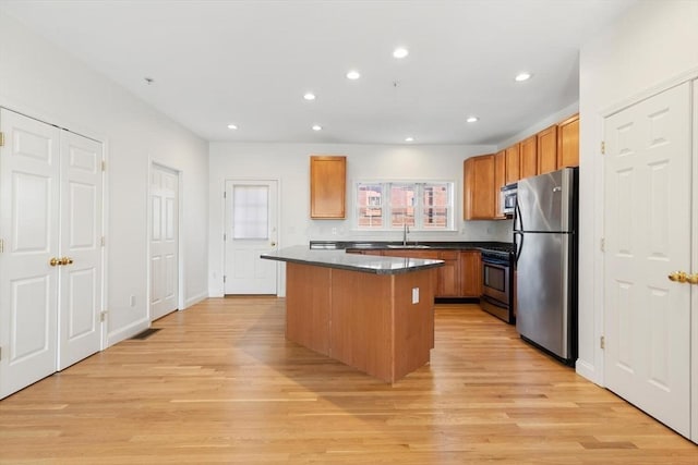 kitchen with light wood-style flooring, appliances with stainless steel finishes, a sink, and a center island