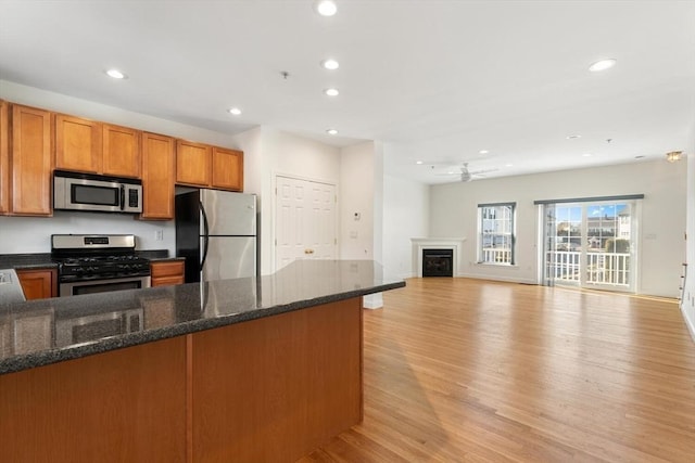 kitchen featuring recessed lighting, stainless steel appliances, a fireplace, light wood-type flooring, and brown cabinetry