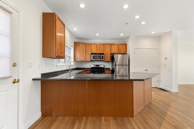 kitchen with stainless steel appliances, brown cabinetry, a sink, light wood-type flooring, and a peninsula