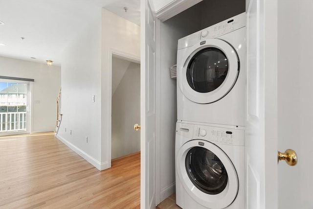 clothes washing area with light wood-style floors, laundry area, baseboards, and stacked washer / drying machine