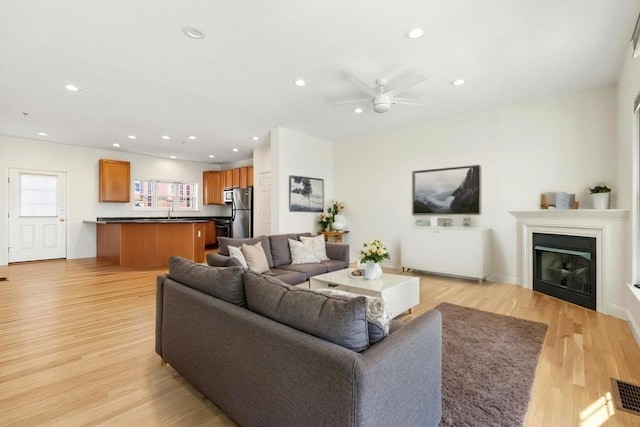 living room with light wood-type flooring, a glass covered fireplace, ceiling fan, and recessed lighting