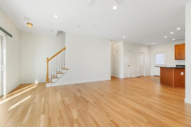 unfurnished living room with stairs, light wood-type flooring, baseboards, and recessed lighting