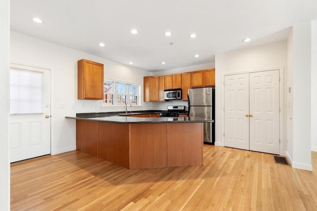 kitchen with dark countertops, stainless steel appliances, a peninsula, and a sink