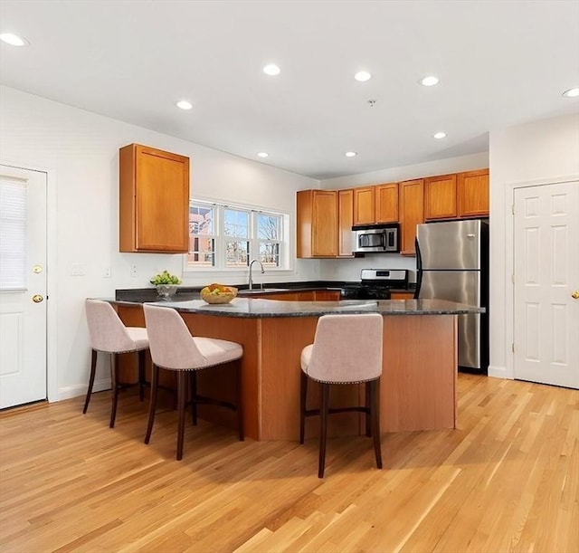 kitchen with a breakfast bar area, recessed lighting, stainless steel appliances, light wood-type flooring, and brown cabinetry