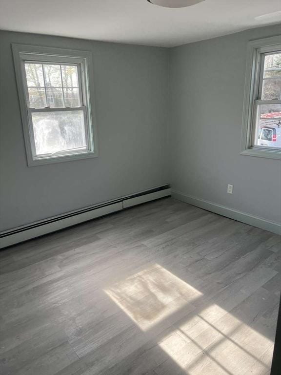 spare room with a baseboard radiator, wood finished floors, and baseboards