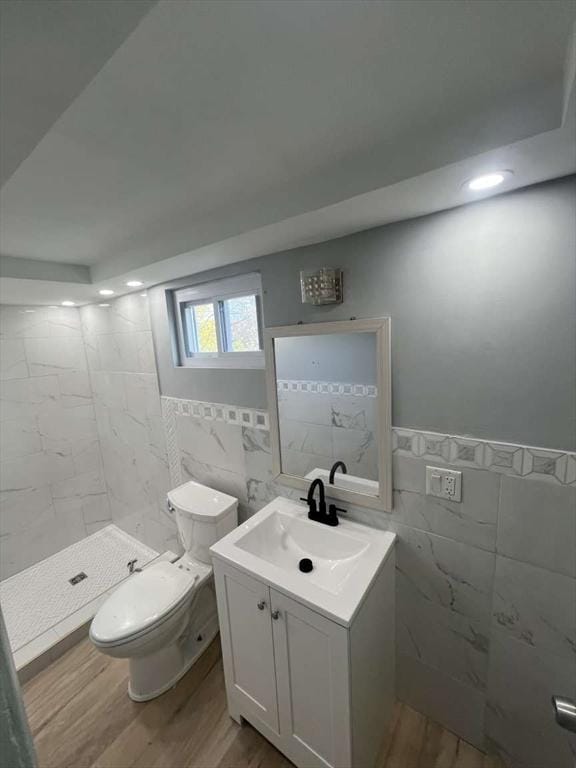 bathroom with wood finished floors, tile walls, toilet, a shower stall, and vanity