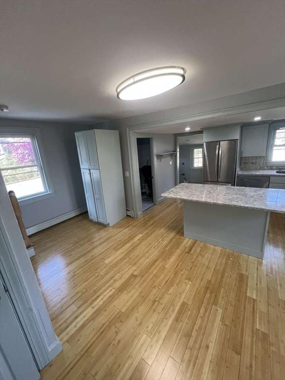 kitchen with freestanding refrigerator, light wood-style floors, light stone counters, a kitchen island, and gray cabinetry
