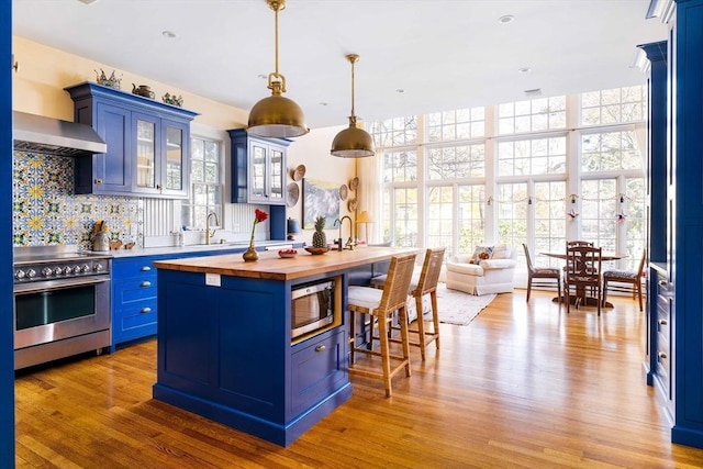 kitchen featuring a breakfast bar, a kitchen island with sink, blue cabinetry, wooden counters, and stainless steel appliances