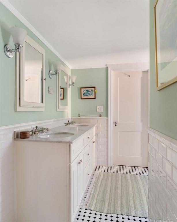 full bathroom featuring double vanity, tile walls, a sink, and a wainscoted wall