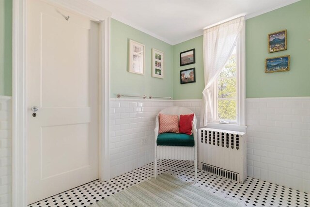 living area featuring radiator heating unit, tile walls, crown molding, and a wainscoted wall